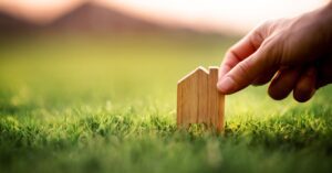 News 5 concept of small estate probate hand touching little wood shape of house in grass